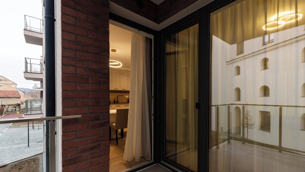 A modern apartment with a sliding glass door leading to a balcony, a visible kitchen area, and a brick exterior wall. - Nest Inn Jasmine Apartment (Oradea)