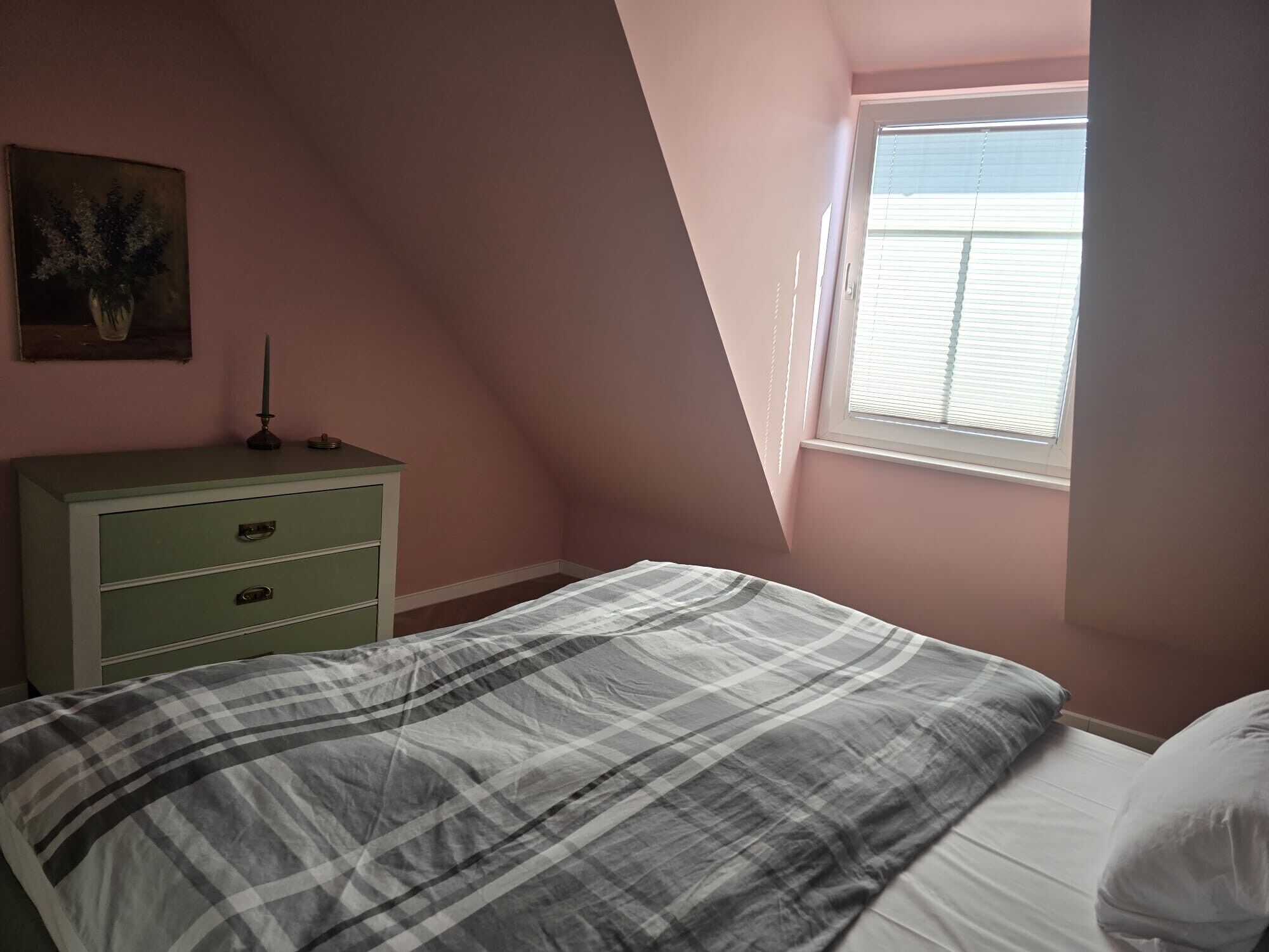 Un dormitorio con cama, cómoda, ventana y un cuadro en la pared.