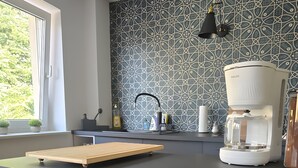 A modern kitchen with a coffee maker, a window with plants, and a patterned backsplash. - Beautiful 2-room apartment in the heart of Taucha (Taucha)