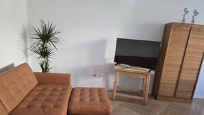 A living room with a sofa, ottoman, TV stand, wooden cabinet, and a potted plant. - Beautiful 2-room apartment in the heart of Taucha (Taucha)