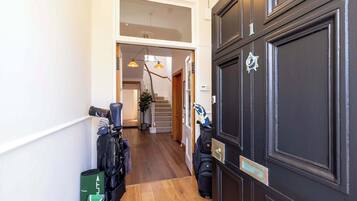Un pasillo con piso de madera, una puerta negra con placa y una escalera que sube a un nivel superior.