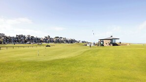 A golf course with a clubhouse, a flag, and a distant town. - Detached House with Sea Views & Parking (North Berwick)