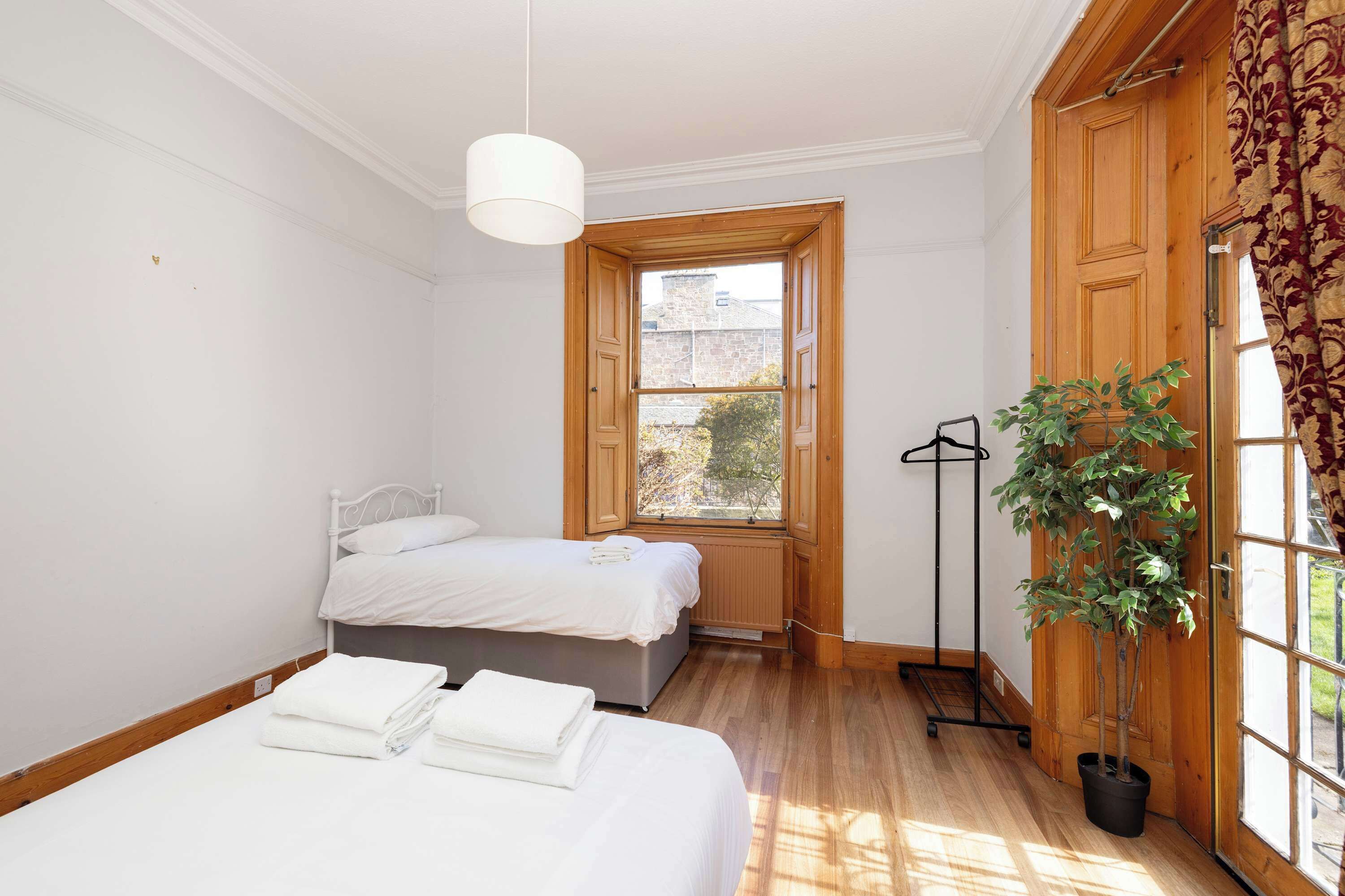 A bedroom with two beds, a radiator, a potted plant, and a window with wooden shutters.