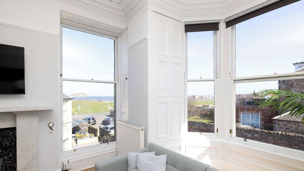 A room with a fireplace, a grey sofa, and large windows with a view of the outside. - Detached House with Sea Views & Parking (North Berwick)