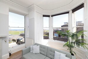 A room with a grey sofa, large windows, and a potted plant.