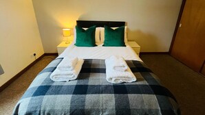 Una camera d'albergo con un letto, due cuscini, un comodino con una lampada e due asciugamani sul letto.