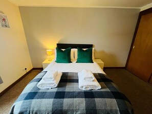Habitación de hotel con cama, dos almohadas, mesita de noche con lámpara y dos toallas sobre la cama.