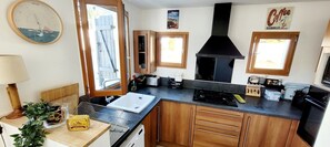 A kitchen with wooden cabinets, a black stove, a sink, and a clock on the wall. - Seaside House with Terrace and Garden – 300m from the Beach (La Tranche-sur-Mer)
