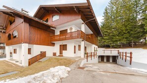 Una casa de madera de varios pisos con balcones, un garaje y una entrada cubierta de nieve.