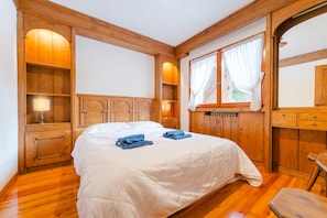 A wooden-framed bedroom with a bed, built-in shelves, and a window with curtains. - Ca' Donatella - Mountain View Terrace  (Cortina d'Ampezzo)