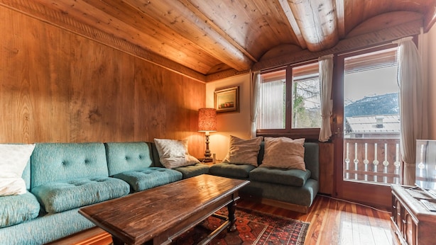Una habitación acogedora con paredes y techo de madera, un sofá verde, una mesa de centro de madera y una ventana con vistas a las montañas.