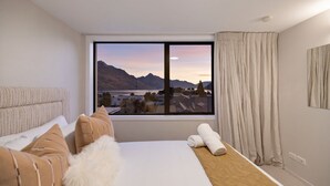 Hotellihuone, jossa on suuri ikkuna, sänky, sohva sekä näkymä vuorille ja järvelle.