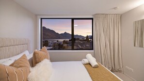 A hotel room with a large window, a bed, a sofa, and a view of mountains and a lake. - Queenstown Hill House - Apartment Only with stunning lake & mountain views. (Queenstown)