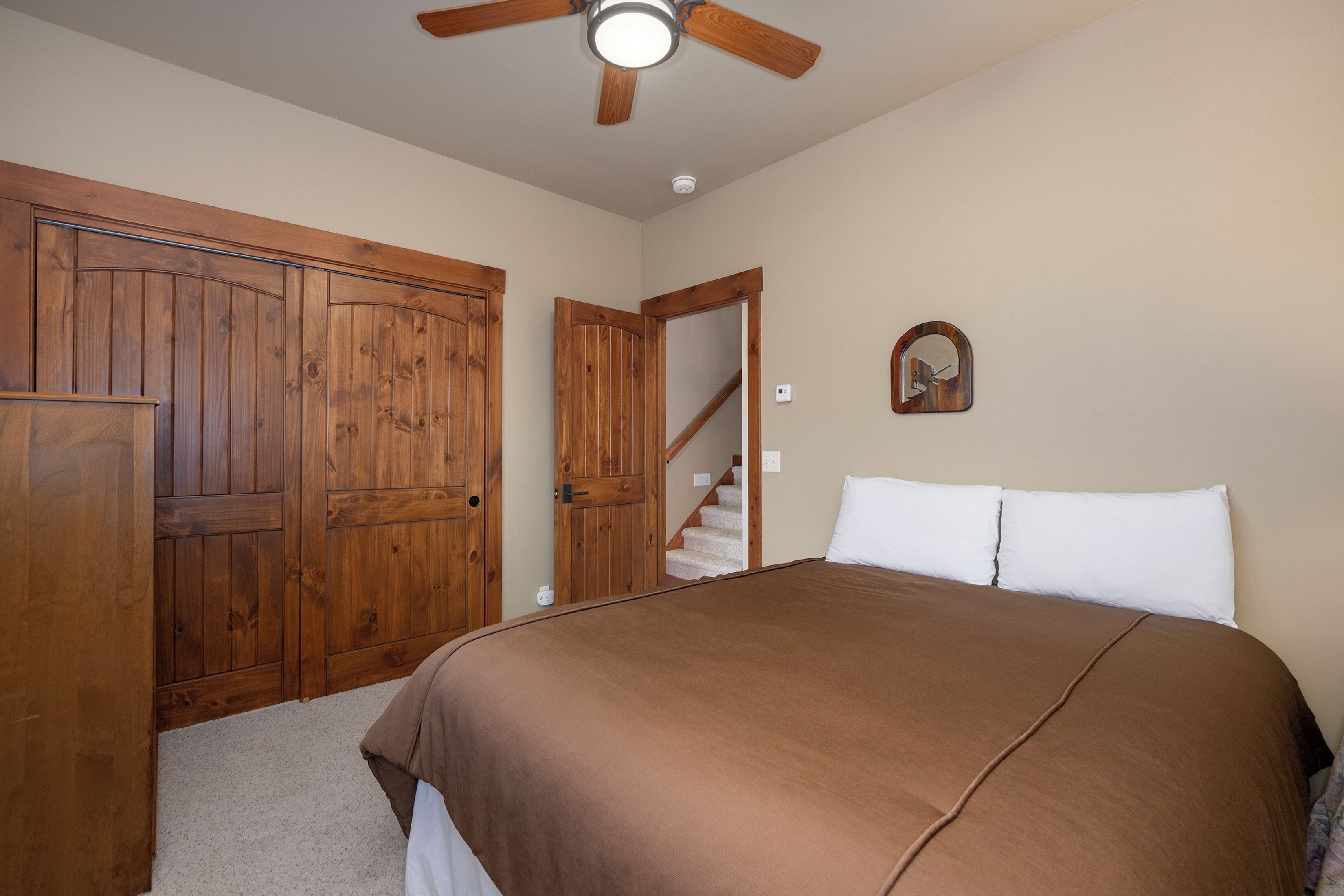 A bedroom with a bed, wooden wardrobe, a ceiling fan, and a staircase.