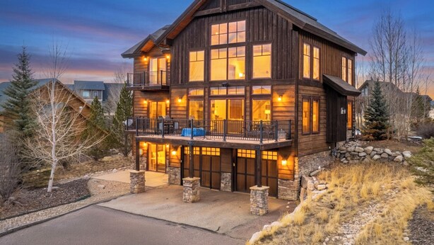 A large, multi-story wooden building with a balcony, stone foundation, and a driveway. - 892 Saddle Ridge Ultra luxurious 4 bedroom home, views, 2 living spaces and more (Granby)