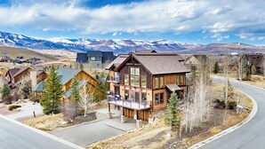 A modern log cabin with a balcony, surrounded by a residential area with mountains in the background. - 892 Saddle Ridge Ultra luxurious 4 bedroom home, views, 2 living spaces and more (Granby)