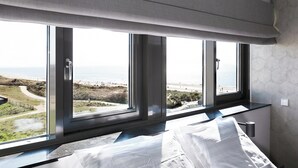 A bedroom with a large window overlooking a beach, a bed, and a nightstand. - Chic Apartment for 8 With Seaview (Egmond aan Zee)