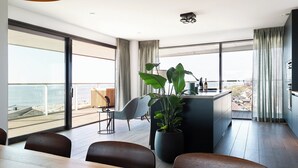 A modern kitchen with a large island, dining area with chairs, and a view of the beach. - Chic Apartment for 8 With Seaview (Egmond aan Zee)