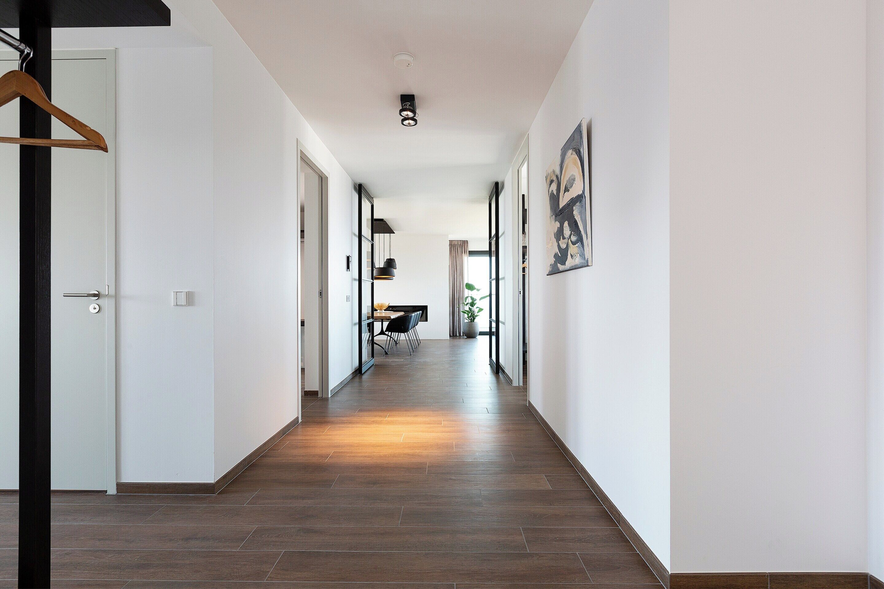 A hallway with a wooden floor, white walls, and a hanging coat rack.