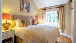 Une chambre à coucher avec un lit, deux lampes de chevet, une fenêtre avec des rideaux, un tableau au mur et un plancher en bois.