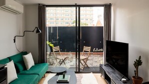 Una sala de estar con un sofá verde, una mesita redonda con un libro, dos sillas de madera, un televisor y una planta en maceta.