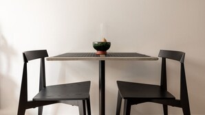 Una mesa con un tazón verde, una vela, dos sillas negras y una pared lisa.
