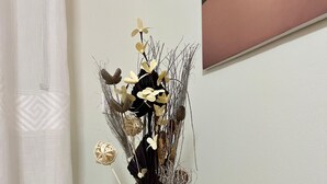 Eine Korbbasi mit gewebtem Muster, gefüllt mit getrockneten Blumen und Blättern, steht auf einem Holzboden vor einer weißen Wand.