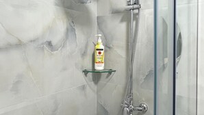 Eine gläserne Duschkabine mit Handbrause und Regendusche, ein Glasregal mit einer Shampoo-Flasche und Wände mit Marmoroptik.