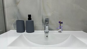 Ein Badezimmerwaschbecken mit modernem Wasserhahn, zwei zylindrischen Behältern und einer kleinen Vase mit Blumen.