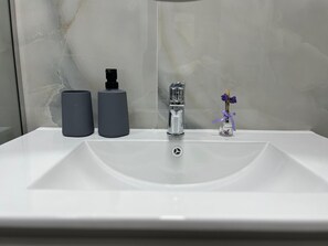 A bathroom sink with a modern faucet, two cylindrical containers, and a small vase with flowers.