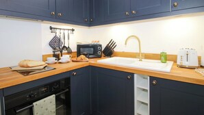 A compact kitchen with dark blue cabinets, a microwave, a toaster, and a sink. - The Blacksmiths Shop (Bromyard)