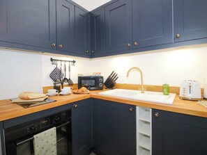 A compact kitchen with dark blue cabinets, a microwave, a toaster, and a sink. - The Blacksmiths Shop (Bromyard)