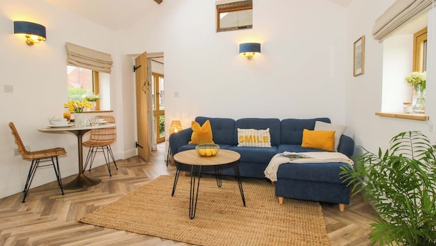 A cozy living room with a blue sofa, a dining table with chairs, a coffee table, and a large window with curtains. - The Blacksmiths Shop (Bromyard)