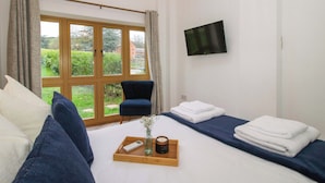A hotel room with a bed, a chair, a TV, and a window with a view of greenery. - The Blacksmiths Shop (Bromyard)