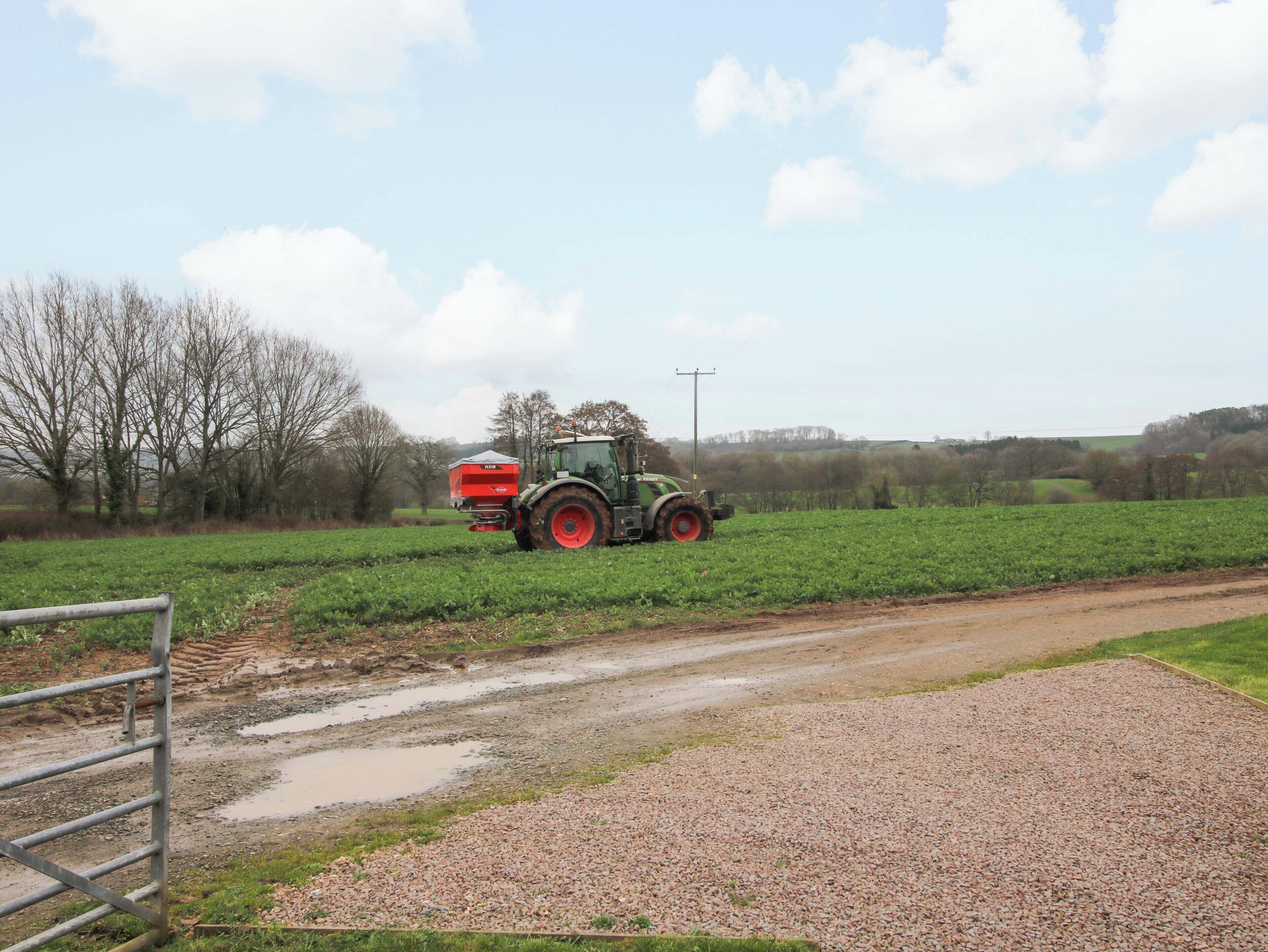 A tractor in a field with a gravel path and a metal gate.
