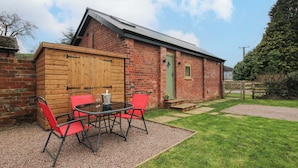 A brick building with a wooden door, a green door, and a small window. There is a table with chairs in front of the building. - The Blacksmiths Shop (Bromyard)
