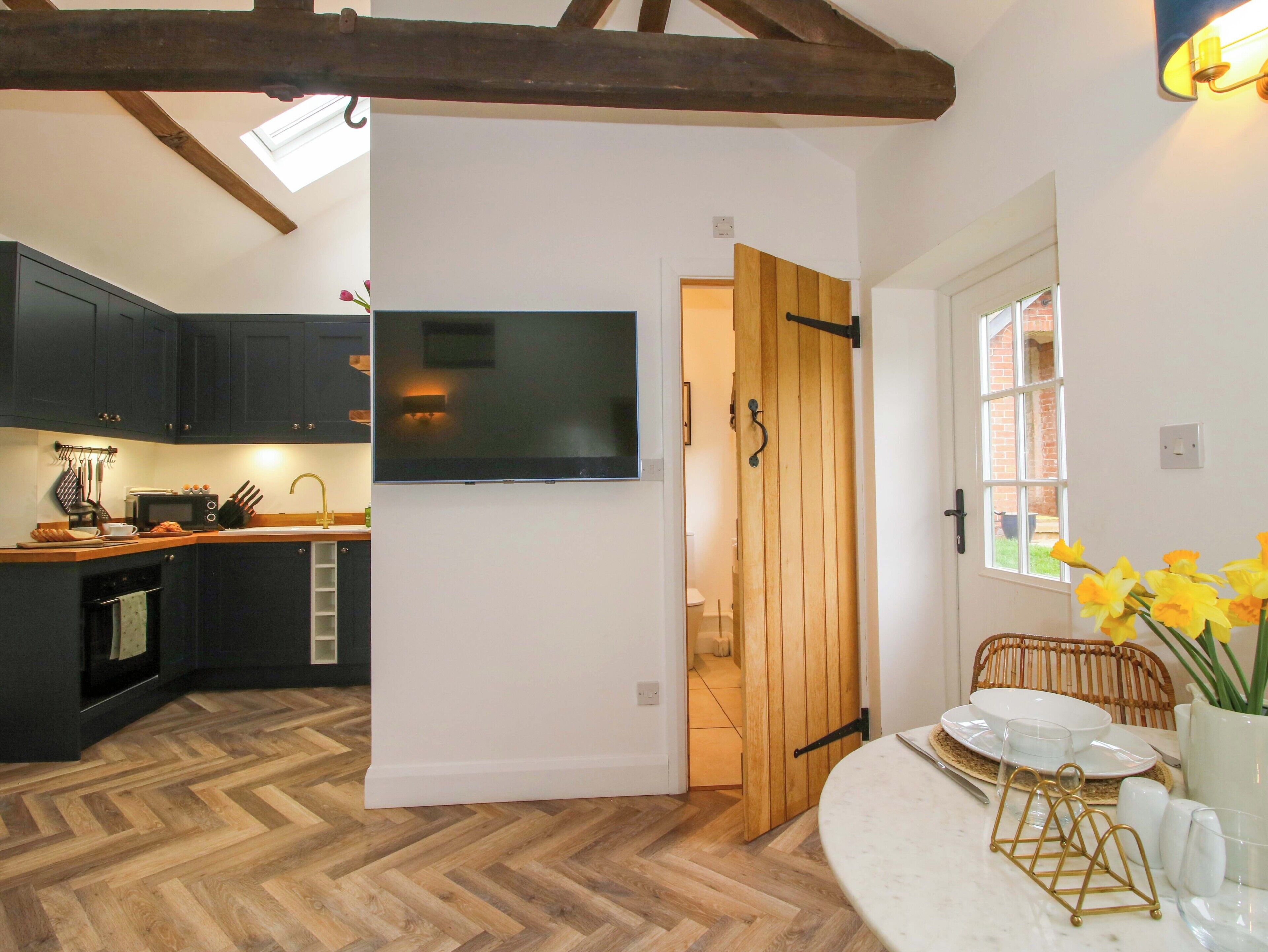 A kitchen with dark cabinets, a flat-screen TV, and a wooden door leading to another room.