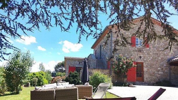A stone building with red shutters, a wicker sofa, and a chair in a sunny outdoor area. - Character house, in a quiet location, close to the village center (Jaujac)