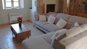 A living room with a stone wall, a sofa, a fireplace, and a window. - Character house, in a quiet location, close to the village center (Jaujac)
