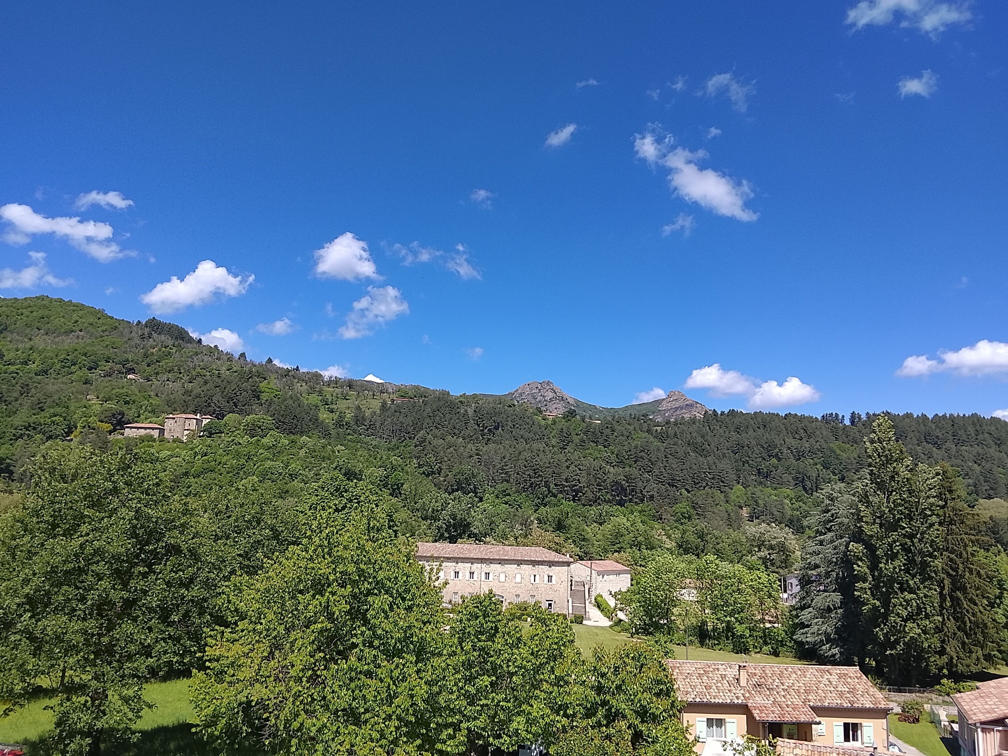 A mountainous landscape with a clear sky, a large building with a tiled roof, and dense greenery.