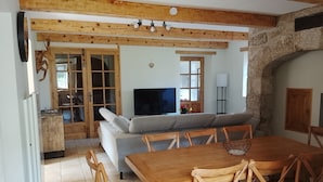 A dining area with a wooden table and chairs, a television, and a stone wall. - Character house, in a quiet location, close to the village center (Jaujac)