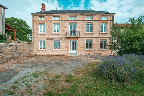 Ein mehrstöckiges Gebäude mit einer steinernen Fassade, einem zentralen Eingang mit einer weißen Tür und einem kleinen Balkon mit Blumen.