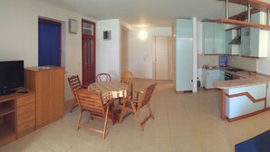 Un espace de vie compact comprenant un coin repas, une kitchenette et un téléviseur posé sur un meuble en bois.