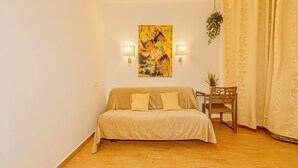 A room with a sofa, a chair, a table, a painting, and two wall-mounted lights. - Studio Apartment 4 pax (Roma)