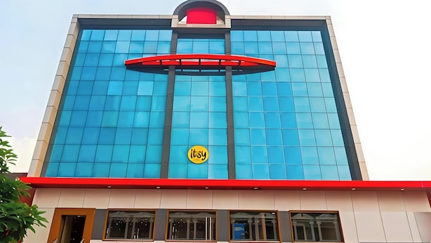 A building with a prominent blue glass facade, a red awning, and a yellow circular logo. - HOTEL Q NESS  (Hyderabad)