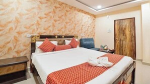 A hotel room with a bed, a nightstand, a chair, a wooden door, and a ceiling fan. - HOTEL Q NESS  (Hyderabad)