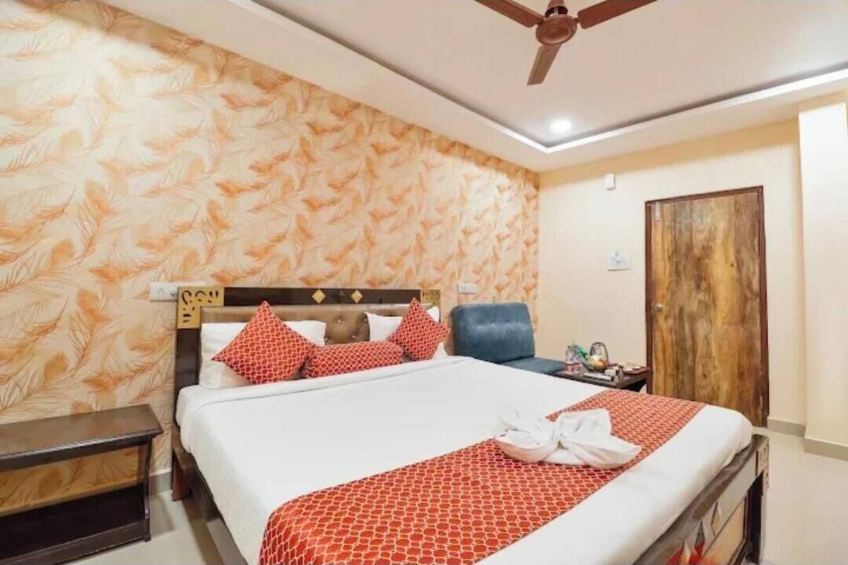 A hotel room with a bed, a nightstand, a chair, a wooden door, and a ceiling fan.