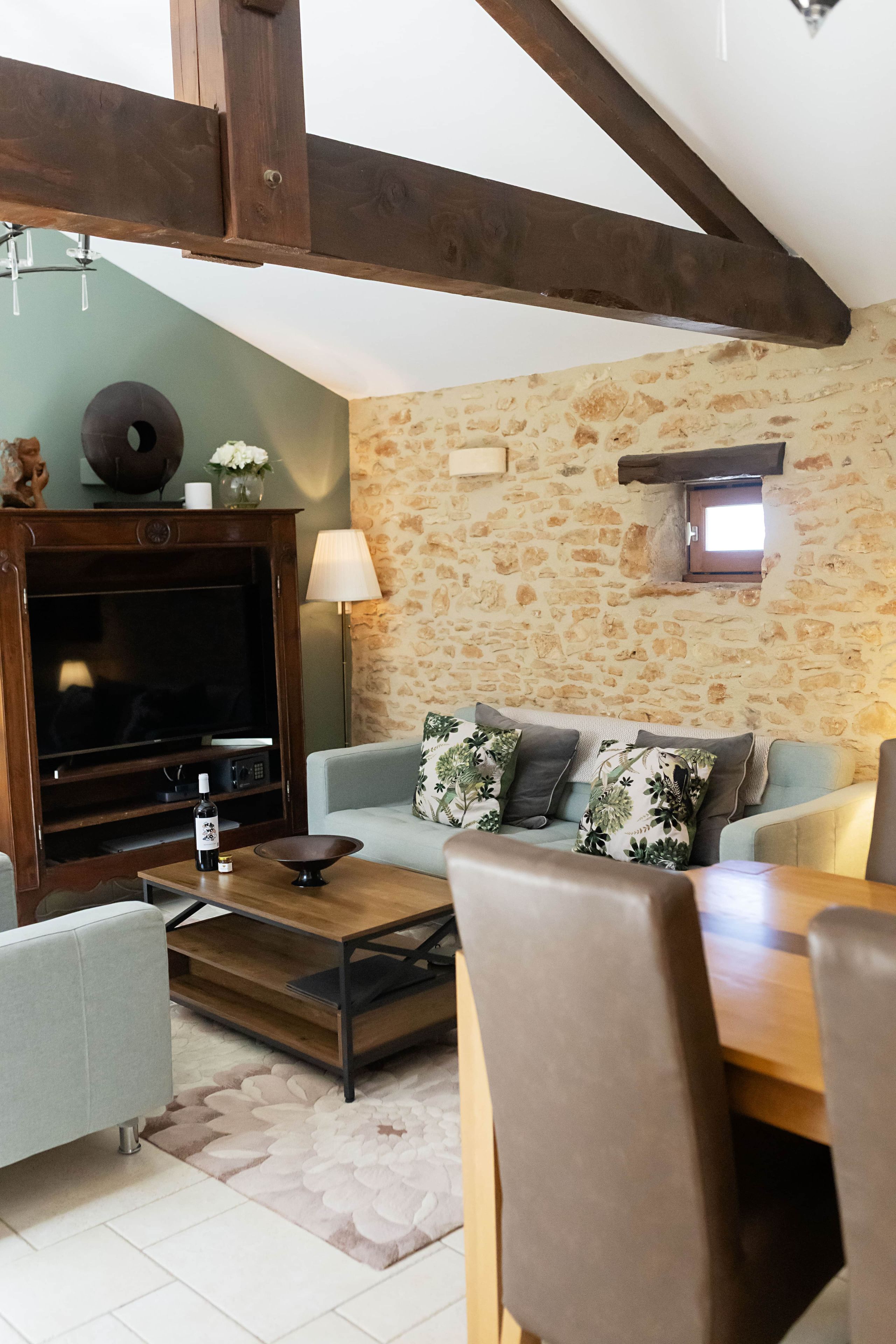 Un salon avec un mur en pierre, un téléviseur, un canapé et une table à manger avec des chaises.