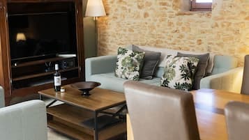 Un salon avec un mur en pierre, un téléviseur, un canapé et une table à manger avec des chaises.