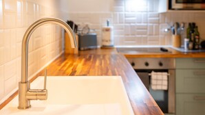 Cozinha moderna com torneira de aço inoxidável, bancada de madeira e painel de azulejos branco.